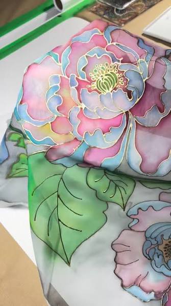 Close-up of hand-painted floral batik fabric with pastel petals, green leaves, and fine resist lines